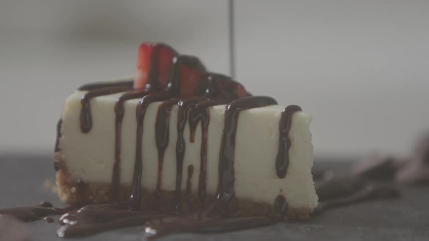 Chocolate sauce is being drizzled over a slice of cheesecake