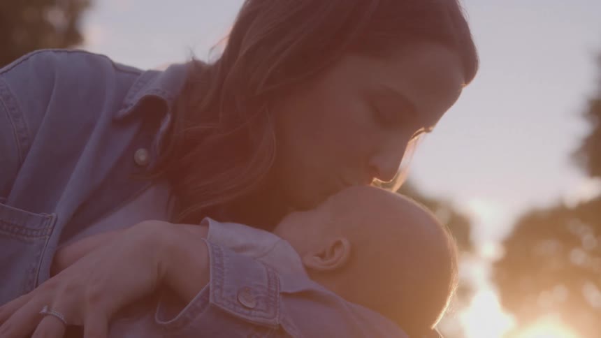 Woman kisses the head of a baby in her arms at sunset