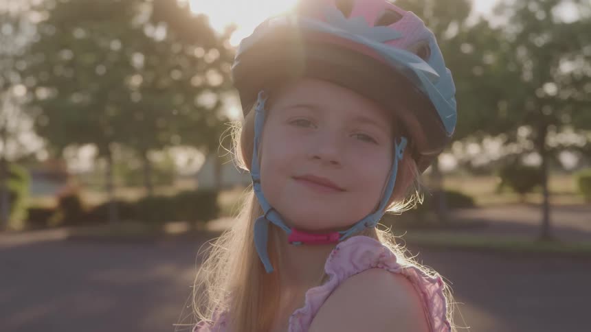 Girl wearing a helmet smiles softly outdoors with the sun in the background
