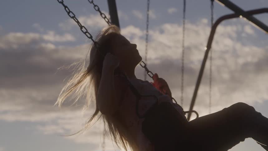 A girl swings in an outdoor suburban play area at sunset
