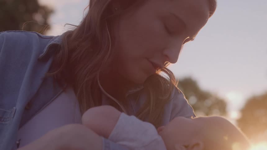 A woman holds a baby in her arms while gently rocking it while outdoors