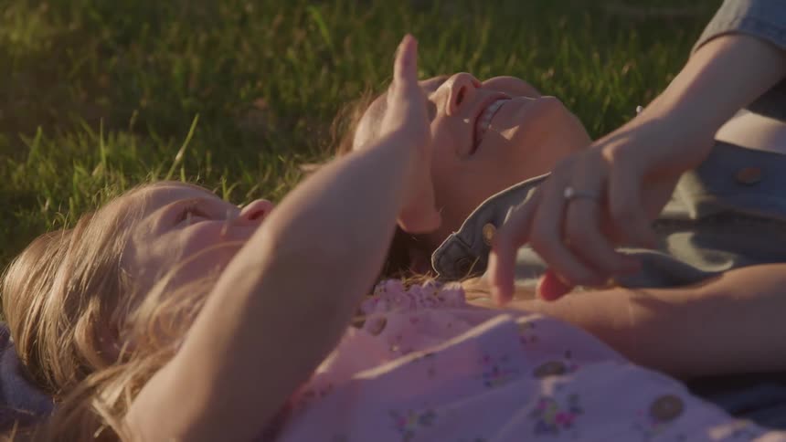 A mother and daughter smile while laying on the grass