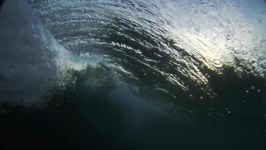 The video shows an underwater perspective of a persons legs and a surfboard in the ocean the camera then goes into a barrel of a wave as it crashes revealing the sunlight from the other side the video has a watermark that reads filmsupply