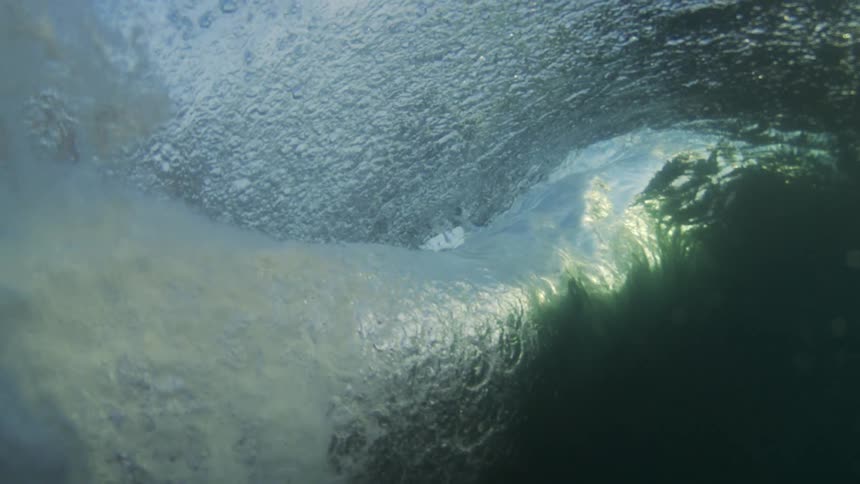 A lone surfer is paddling on their board as a large ocean waves comes crashing down