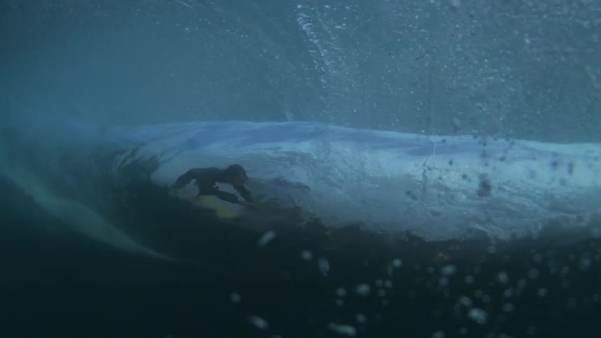 A large ocean wave crashes down and the silhouette of a person can be seen