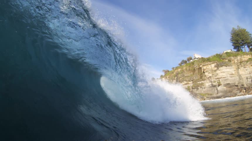 Large wave forming in the sea under a blue sky with thin clouds