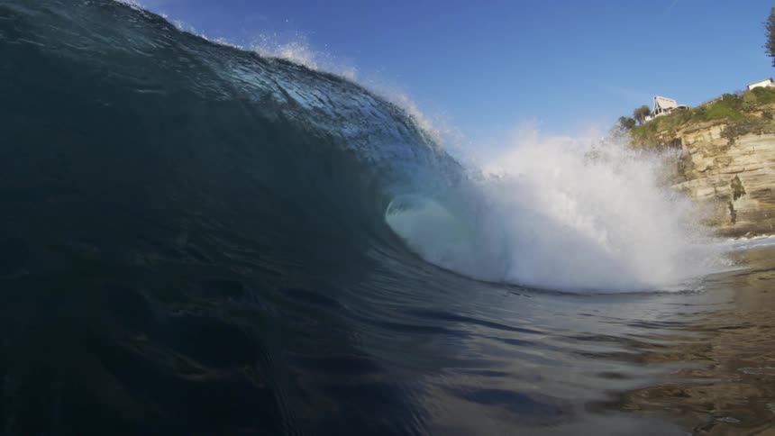 Huge wave crashing near cliffs under a blue sky
