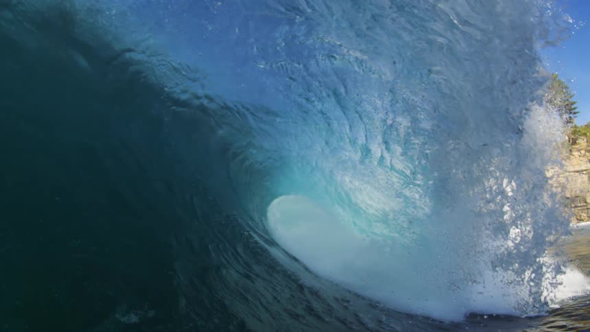 Surfboard tumbles out of a huge wave splashing as it rolls into shore and the view goes underwater