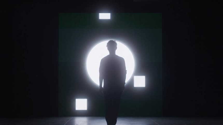 The man walks as large lights flash behind him