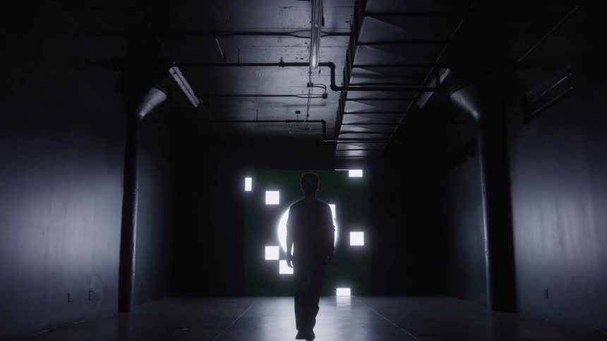 The silhouette of a person walking in an indoor environment that is completely dark with white lights flashing in the background