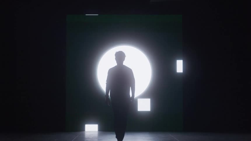 The video shows a person standing in a dark room they are backlit by a large circular light that pulses in a hypnotic way smaller square lights arranged around them also turn on and off in a pattern the words filmsupply are visible as a waterma