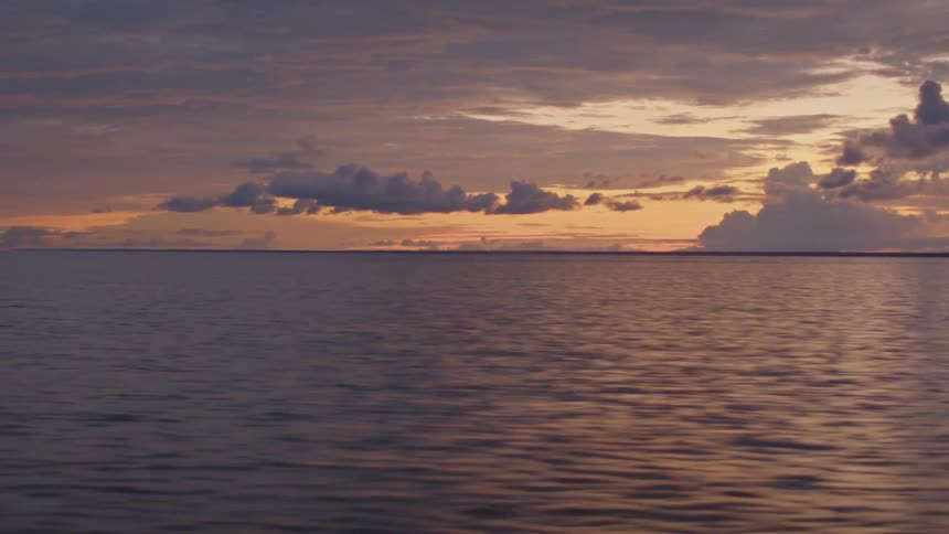 Moving across the water under a colorful cloudy sunset sky as sunlight reflects on the ripples and waves