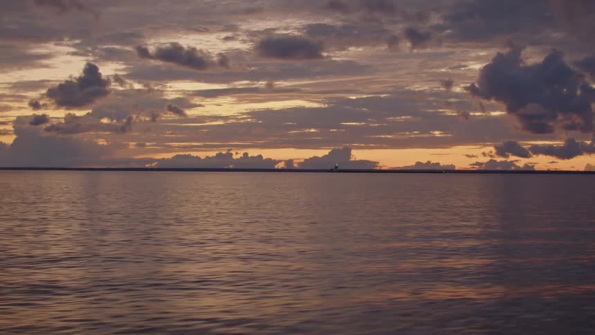 Calm sea reflects orange hues of the sunset with scattered clouds on the horizon
