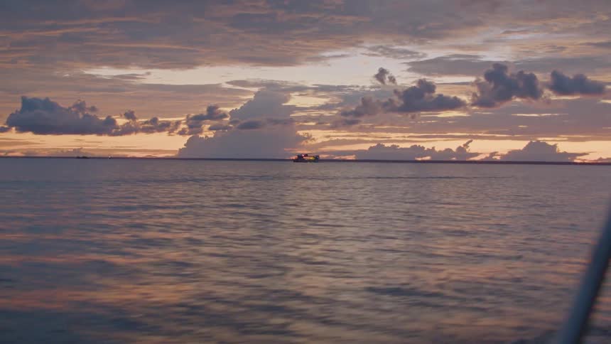 A wide view from the front of a boat shows the vast choppy surface of a body of water under a twilight sky with scattered clouds