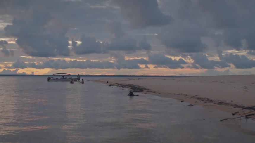 A sandy beach stretches into the ocean under dramatic evening clouds
