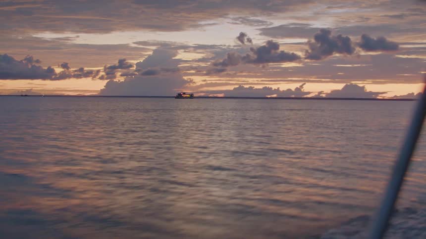 Boat sails on the horizon during sunset over the calm sea