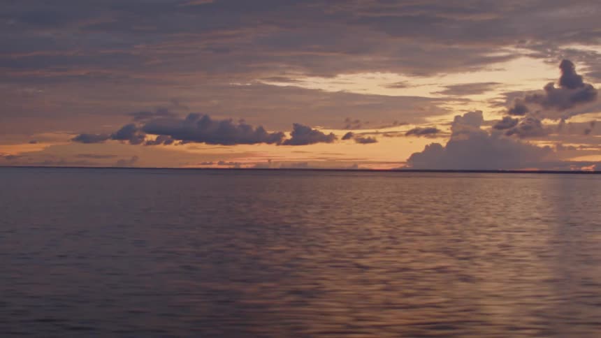 The calm surface of the ocean and the colorful clouds in the sky during a peaceful sunset