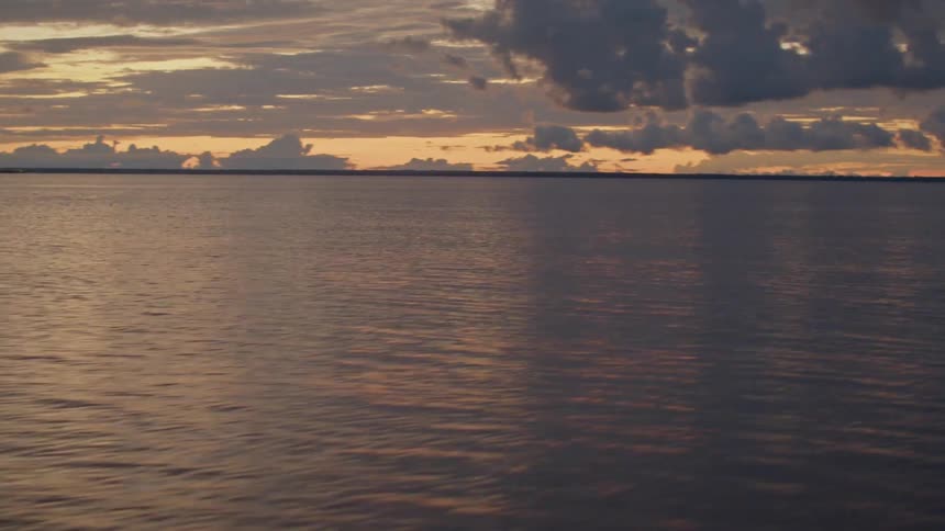 Moving across the water under a dark cloudy sunset sky as a man drives the boat