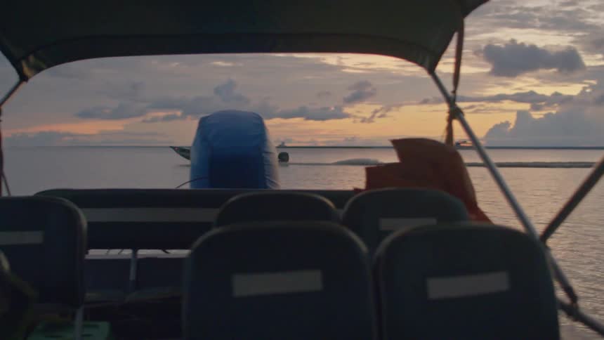 Boat sailing on a lake at sunset seen through the structure of another vessel