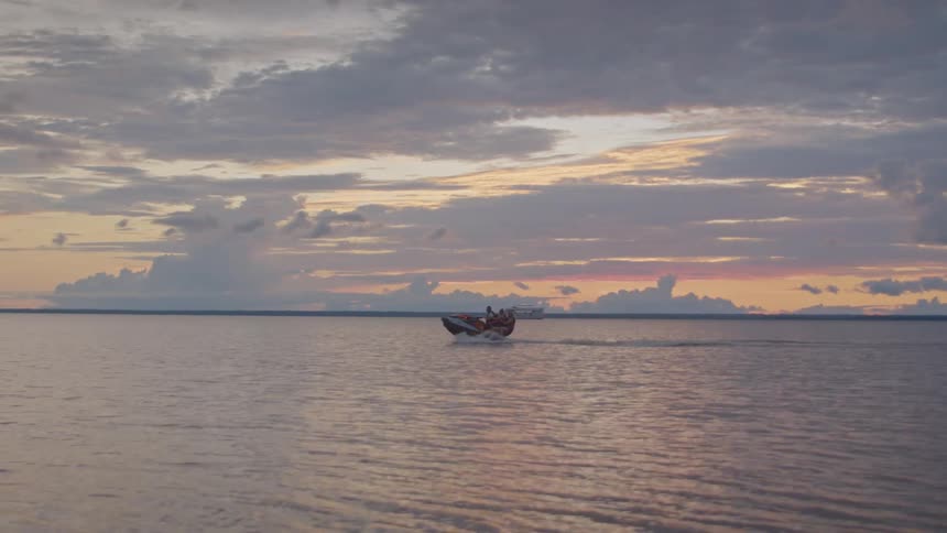 A group of people riding a speedboat from the shoreline into the ocean at sunset
