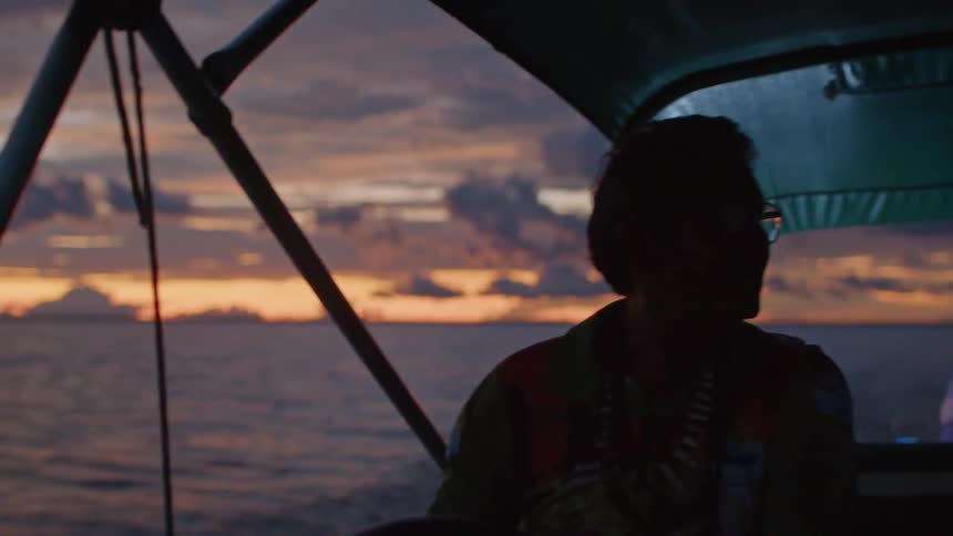 A man navigates his motorboat across the ocean waters at sunset