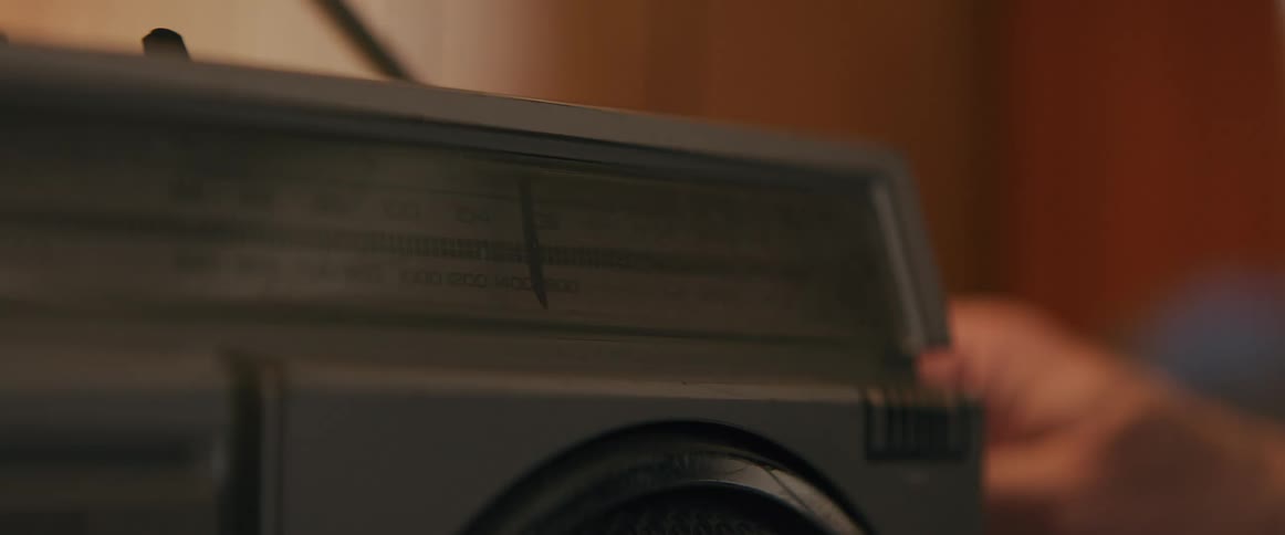 The video shows a hand slowly turning a knob on an old gray radio as the dial moves across the am and fm frequencies the persons face is not visible but the action suggests they are searching for a station