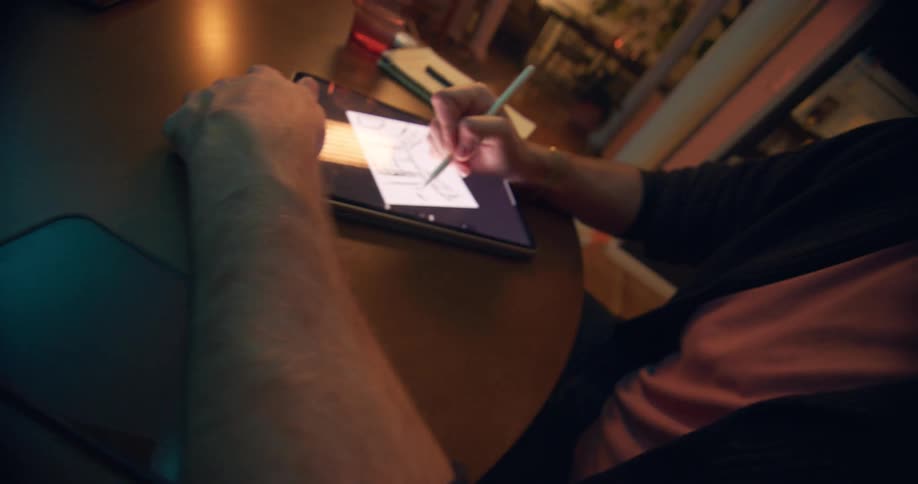 Person draws on a tablet with a digital pen while resting on a table