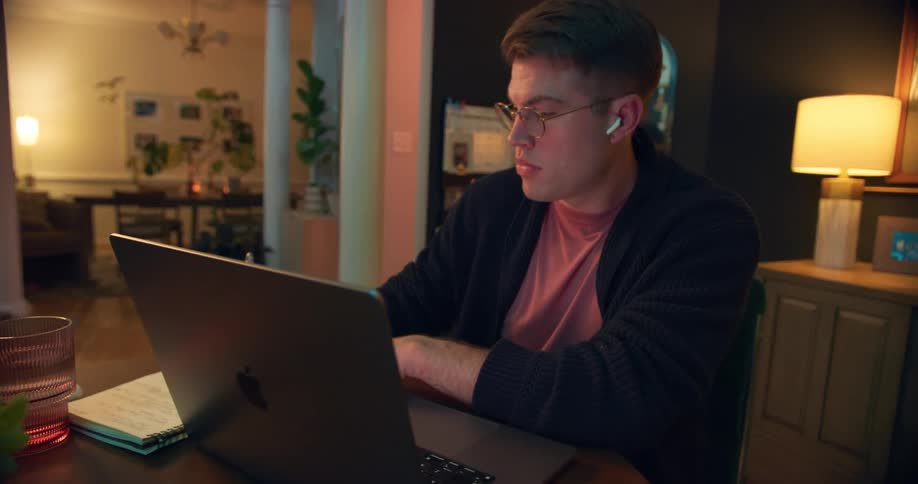 Man wearing earphones works on a laptop at the table