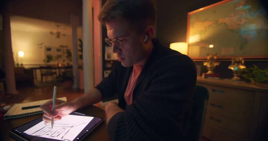 A man sitting at a table draws on the screen of his tablet computer with a stylus