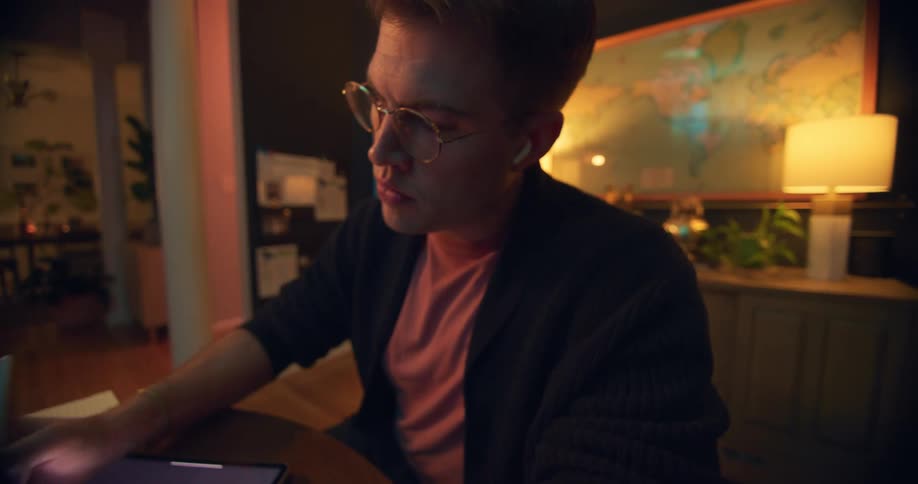 A person is focused on digitally drawing on a tablet in a home office setting while wearing headphones and glasses