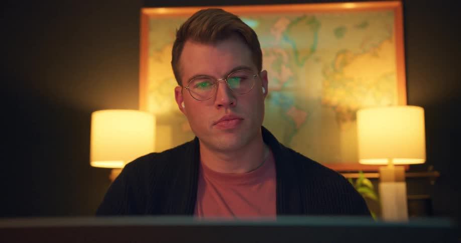 Man with glasses looks straight ahead in a room lit by lamps