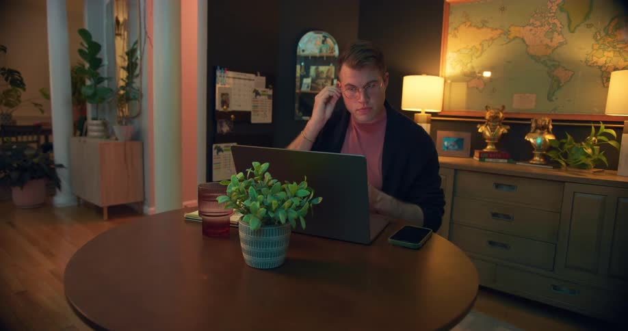 A man works on a laptop at a table in a cozy home office