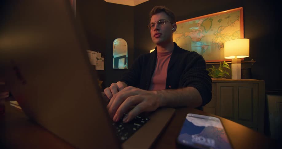 Man pauses work at a laptop looks at his phone and laughs out loud