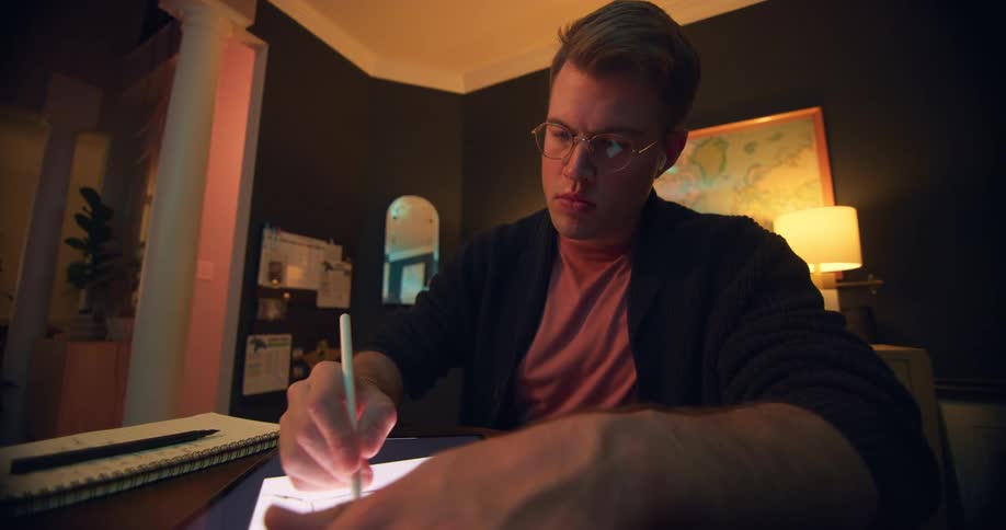 A man sketches on a digital tablet in a cozy home office