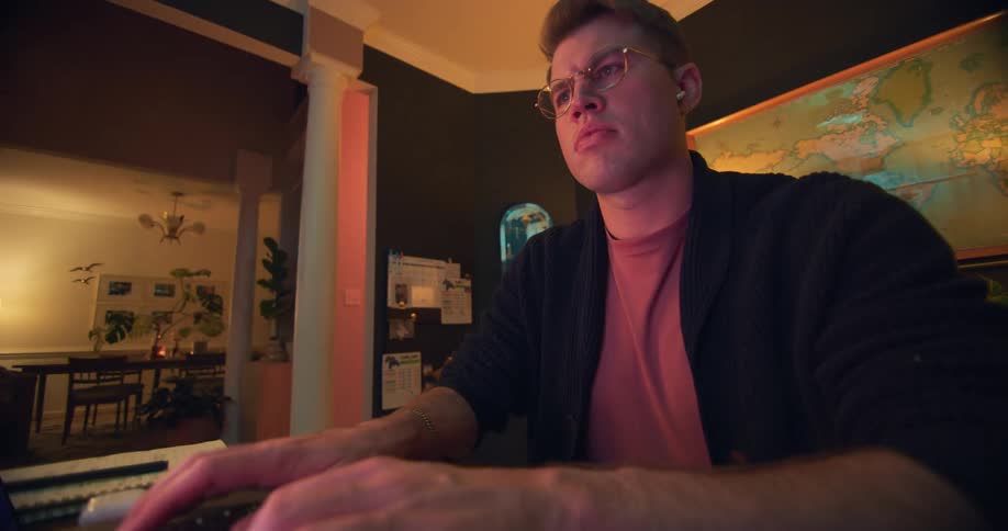 White man wearing glasses sitting down indoors and typing on a laptop computer