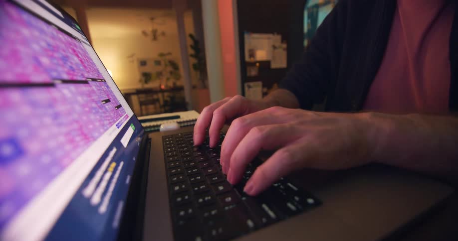 A man is seated at a table where he types on his laptops keyboard
