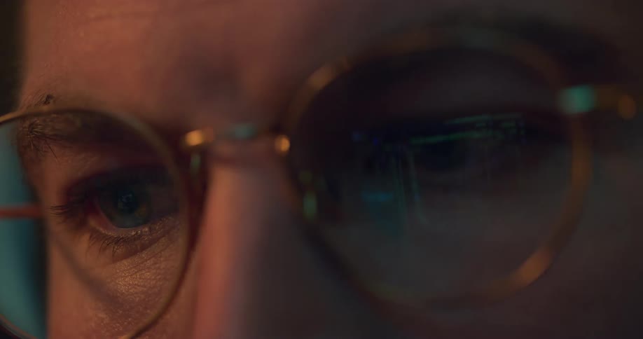 A man looks at his laptop as the reflection of its screen is seen in his glasses