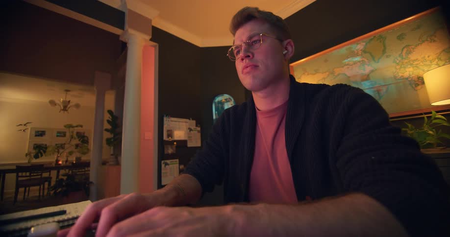 A young man wearing glasses sits and types on his laptop keyboard