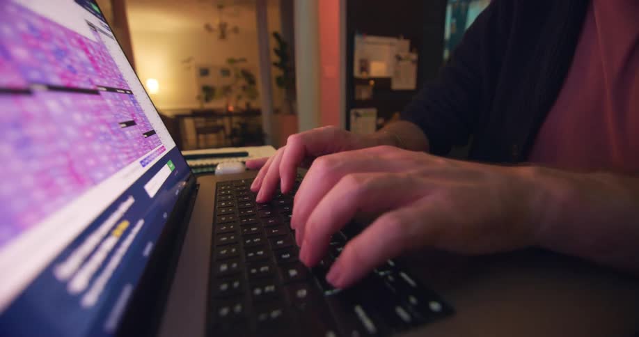 A man sitting at a table with his laptop is typing on its keyboard