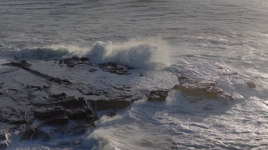 Waves roll into shore and splash against the rocky coast