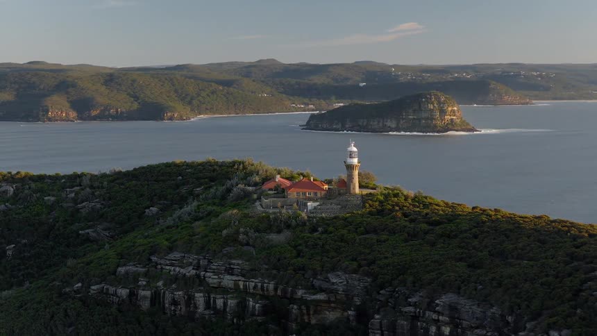 Lighthouse situated on a peninsula surrounded by sea and mountains in the background