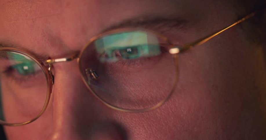 Eyes focused behind glasses with a screen reflection glowing