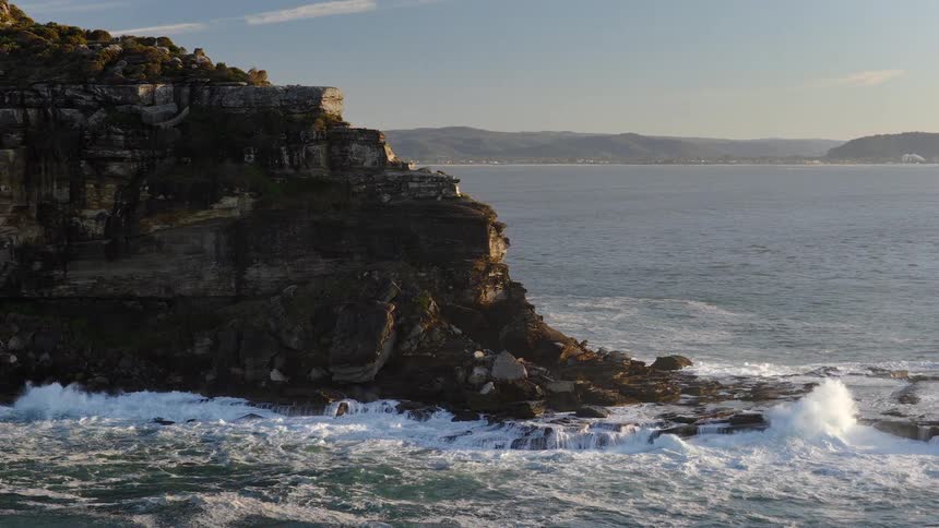 Rocky cliff next to the ocean on a coastal area surrounded by hills during dusk or dawn