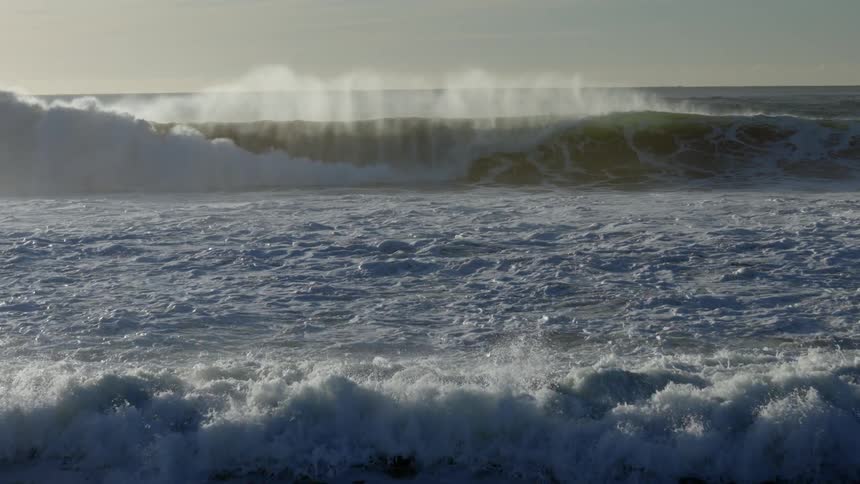 Several large ocean waves come crashing down upon the shoreline