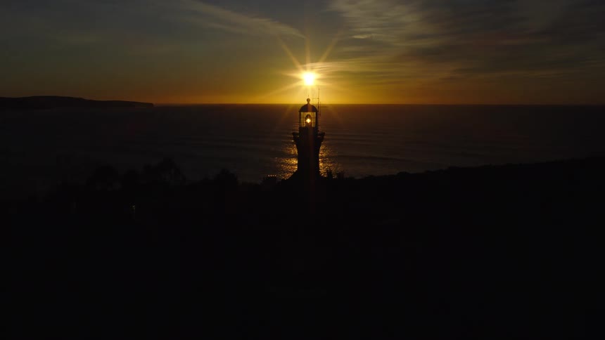 A lighthouse silhouetted against the ocean at sunset