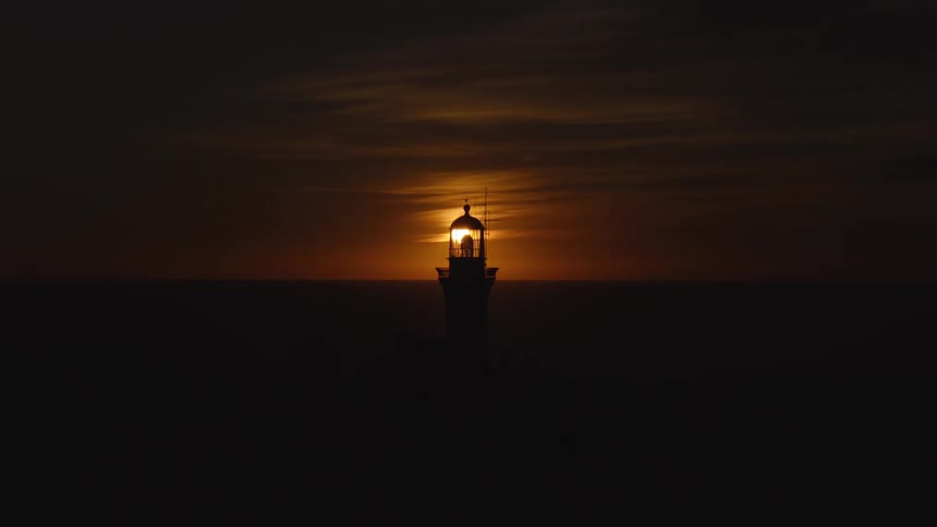 Lighthouse in silhouette against the sunset on the horizon