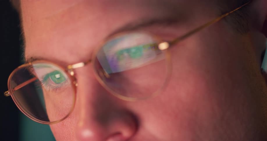 A man wearing glasses focuses his attention on a computer screen