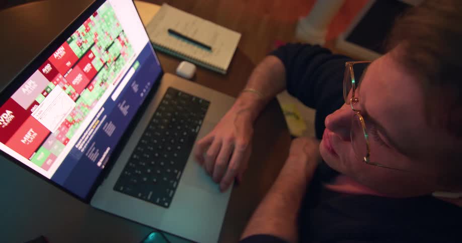 A man wearing glasses is seated at a table while using his laptop computer