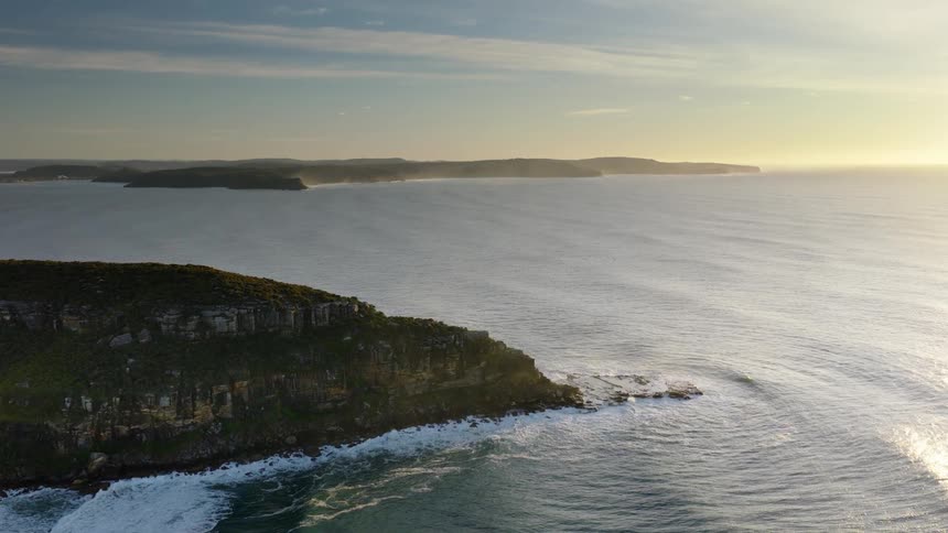 A dramatic coastal cliff rises above the ocean at sunset