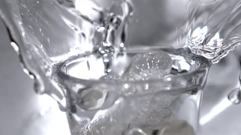 Ice cube falling over a cup of water and water splashing around indoors